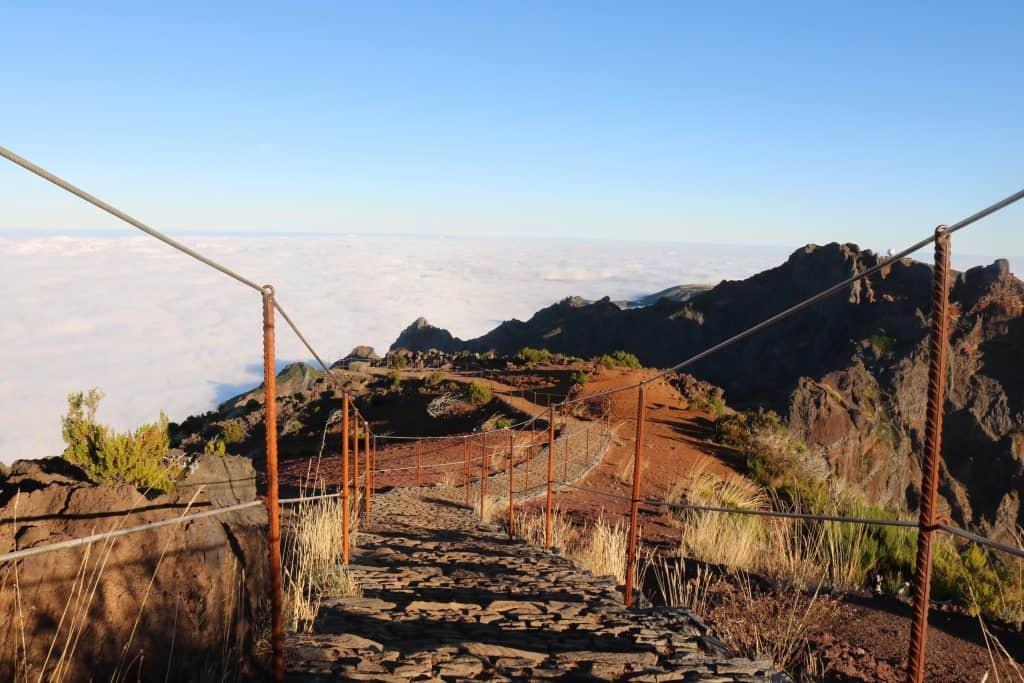 Paved hiking path going down into a sea of clouds and blue sky